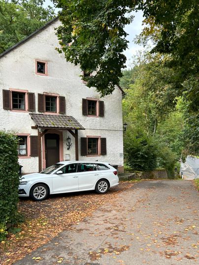 Ein charmantes Haus umgeben von Bäumen. Vor dem Haus steht ein weißes Auto.