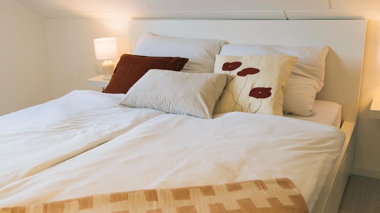 Ein gemütliches Schlafzimmer mit einem großen Bett und mehreren Kissen. Sanftes Licht von einer Nachttischlampe schafft eine einladende Atmosphäre.