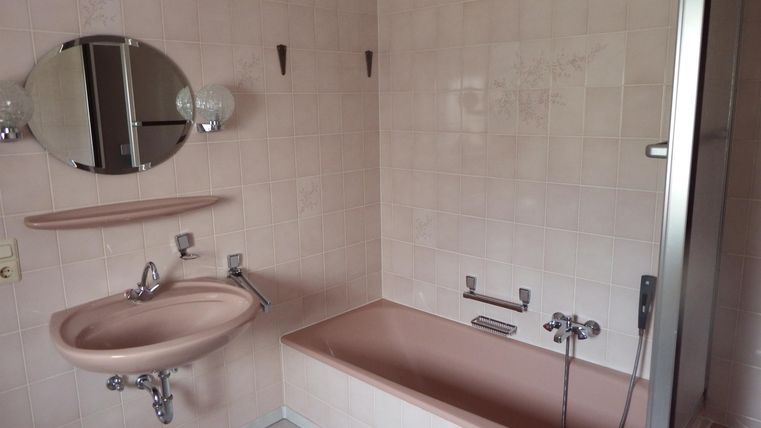 Ein Badezimmer mit einer Badewanne, einem Waschbecken und einer Dusche. Die Wände sind hell gefliest und das Licht ist diffus.