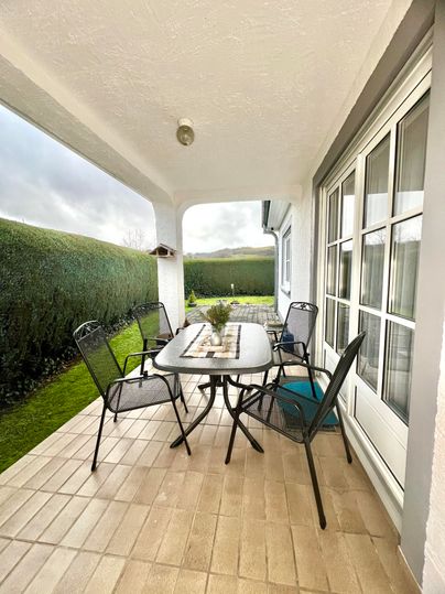Ein gemütlicher Außenbereich mit einem Tisch und Stühlen. Umgeben von grünen Hecken und einer ruhigen Atmosphäre.