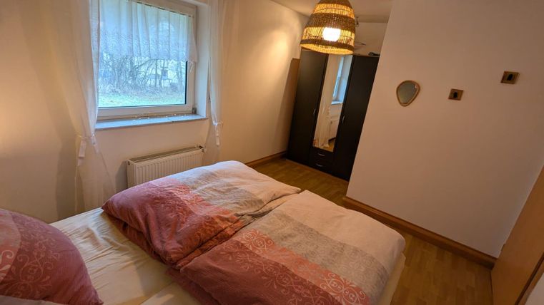 Ein gemütliches Schlafzimmer mit zwei Betten und weichen, bunten Bettdecken. Das Zimmer hat ein Fenster mit Vorhängen und eine warme Beleuchtung durch eine schöne Lampe.