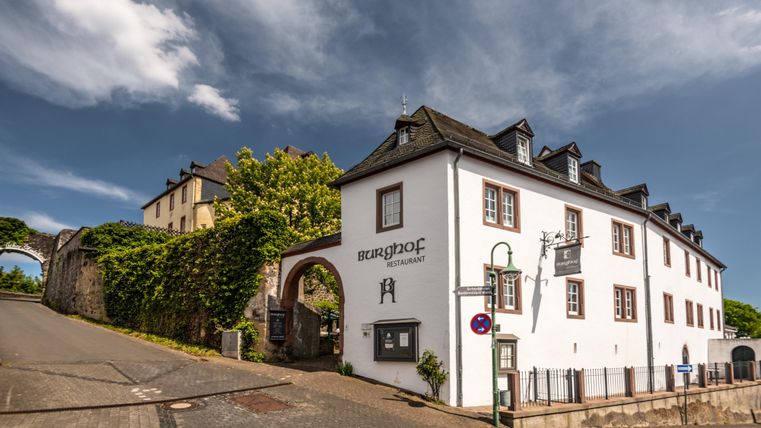 Ein historisches Gebäude mit einer hellen Fassade und einem schönen Eingang. Im Hintergrund sieht man grüne Bäume und einen blauen Himmel.