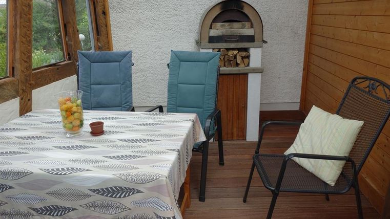 Ein gemütlicher Raum mit einem Tisch und Stühlen. Ein Holzofen und eine Obstschale verleihen dem Ambiente eine einladende Atmosphäre.
