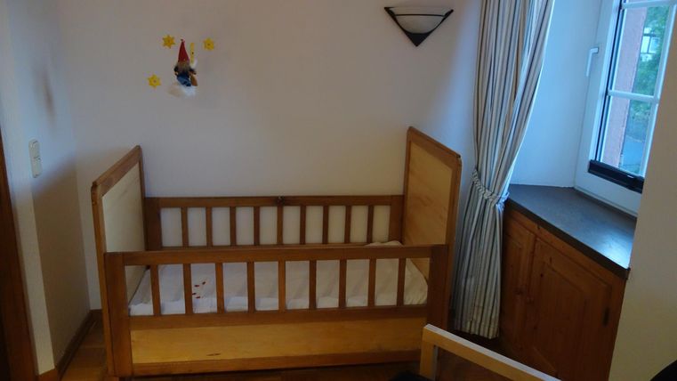 Ein gemütliches Kinderzimmer mit einem hölzernen Kinderbett und einem Fenster. Es gibt helle Wände und eine ruhige Atmosphäre.