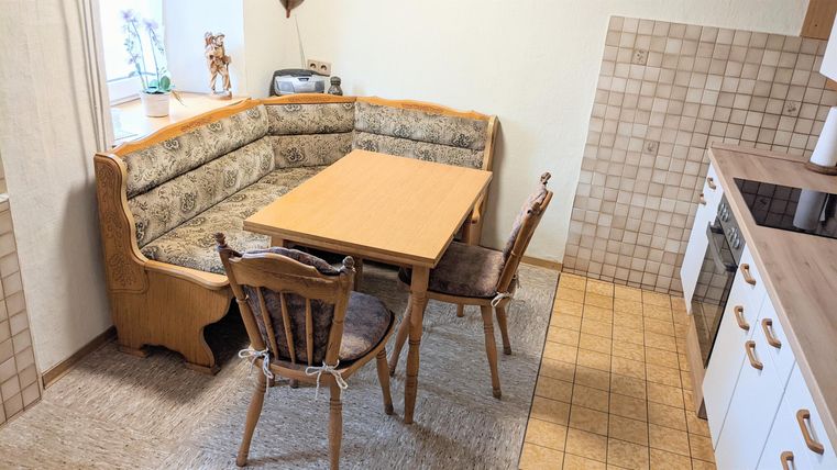 Eine gemütliche Küche mit einer U-förmigen Sitzecke und einem Tisch in der Mitte. Es gibt Holzstühle und eine helle, freundliche Atmosphäre.