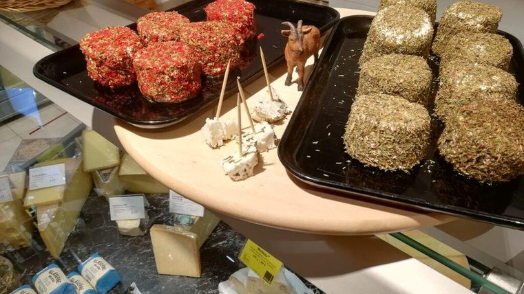 Eine Auswahl an Käse in verschiedenen Sorten, einen Teil mit Kräutern und einen anderen mit Gewürzen. Auf einem Holzbrett stehen einige Käsewürfel und eine kleine Figur.