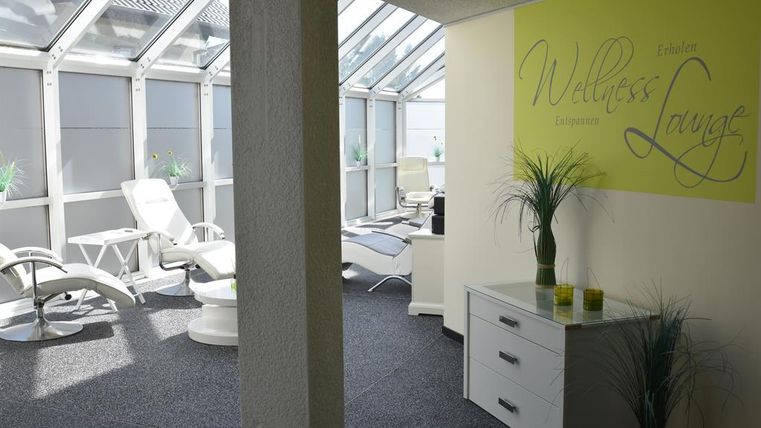 Ein heller Wellness-Bereich mit Liegestühlen und großen Fenstern. Die Wände sind in sanften Farben gehalten, und Pflanzen sorgen für eine entspannte Atmosphäre.