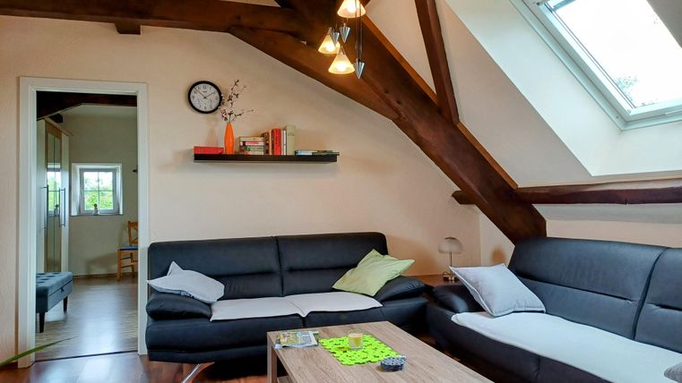 Ein modernes Wohnzimmer mit einer hohen Holzdecke und großen Fenstern. Zwei gemütliche Sofas und ein Tisch schaffen eine einladende Atmosphäre.