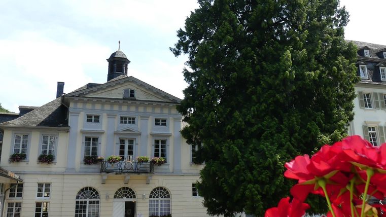 Ein schönes Gebäude mit einem hohen Baum im Vordergrund. Bunte Blumen verschönern die Szene.