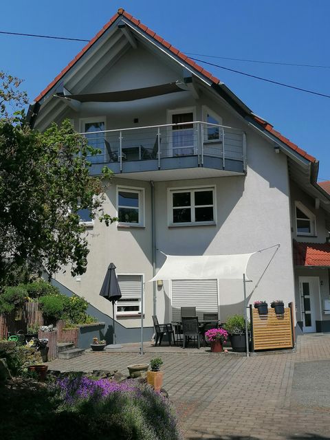 Ein modernes Haus mit einem Balkon und einem schönen Garten. Es gibt einen Sitzbereich im Freien unter einem Sonnenschirm.