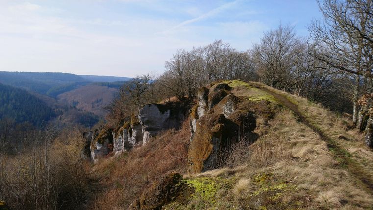 Eine beeindruckende Felsformation mit einer Aussicht auf das grüne Tal. Der Himmel ist klar und die Landschaft zeigt eine Mischung aus bewaldeten Hügeln und freiem Gelände.