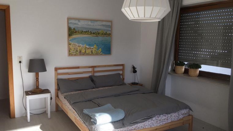 Ein gemütliches Schlafzimmer mit einem Doppelbett und einer hellen Lampe. An der Wand hängt ein Bild einer Landschaft, und es gibt Pflanzen auf der Fensterbank.