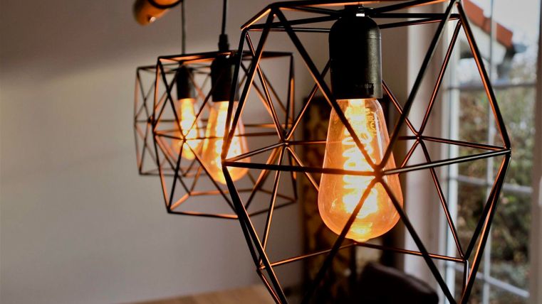 Drei geometrische Lampen mit warmem Licht hängen von der Decke. Der Hintergrund ist hell und homely.