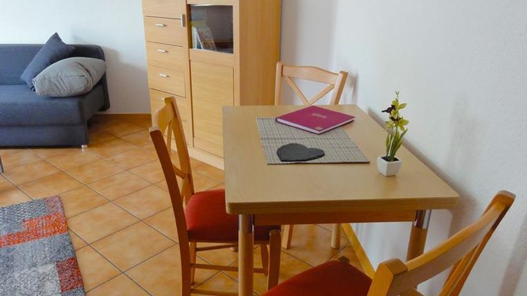 Ein gemütlicher Wohnbereich mit einem kleinen Tisch und Stühlen. Im Hintergrund steht ein Schrank und eine Couch.