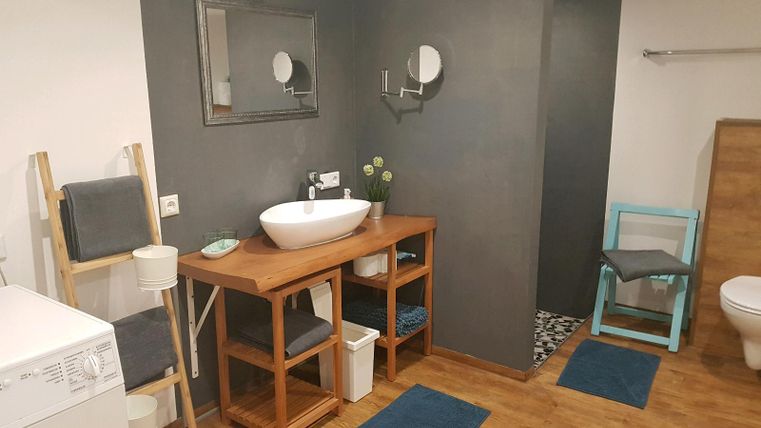 Ein modernes Badezimmer mit Holzregalen und einer großen Waschbecken. Der Boden ist aus Holz, und es gibt einen modernen Toilettenbereich.