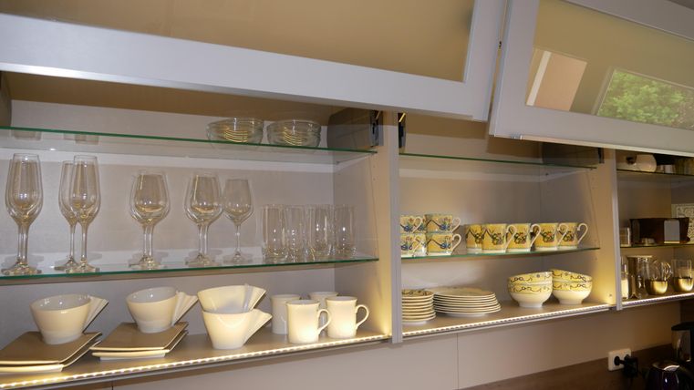 Eine moderne Küchenauslage mit verschiedenen Gläsern und Geschirr. Oben sind elegante Weingläser und darunter bunte Tassen und Teller arrangiert.