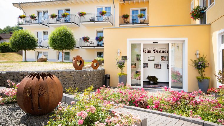 Ein einladender Eingangsbereich mit bunten Blumen und gepflegtem Garten. Im Hintergrund ist ein helles, mehrstöckiges Gebäude zu sehen.