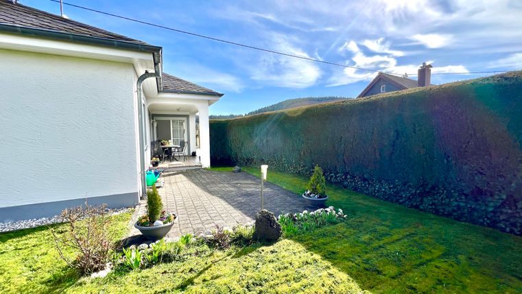 Ein einladender Garten mit grünem Rasen und gepflastertem Weg. Im Hintergrund ist ein helles Haus und eine schöne Himmelsszenerie zu sehen.