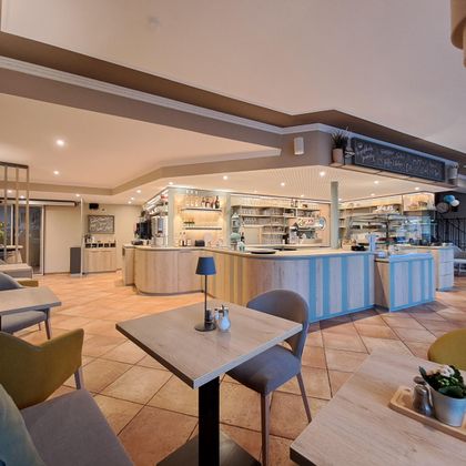 Ein modernes Café mit hellem Innenraum und einer einladenden Theke. Bequeme Stühle und Tische schaffen eine gemütliche Atmosphäre.