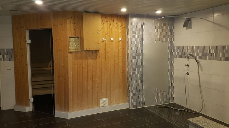 Ein moderner Wellnessbereich mit einer Holzsauna und einer Duschzone. Der Raum hat einen eleganten Fliesenboden und ist angenehm beleuchtet.
