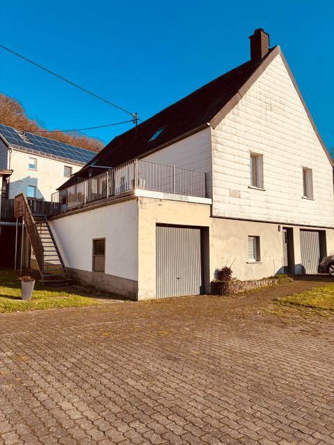 Ein modernes Haus mit einer hellen Fassade und einem Balkon. Der Garten ist gepflegt und die Umgebung ist klar und sonnig.
