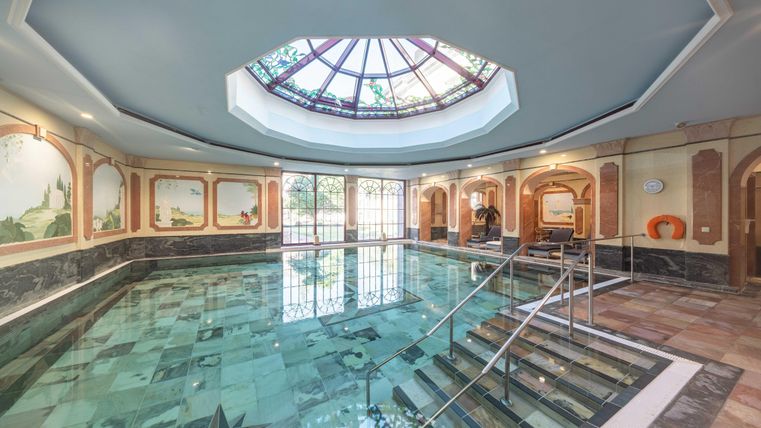 Ein elegantes Schwimmbad mit einem kunstvollen Oberlicht und stilvollen Wänden. Die Wasseroberfläche spiegelt die Umgebung wider und sorgt für eine entspannende Atmosphäre.