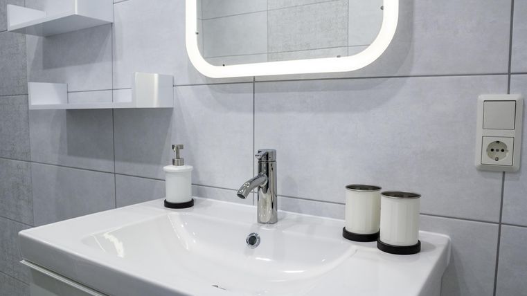 Ein modernes Badezimmer mit einem eleganten Waschbecken und einem Spiegel. Dazu gehören dekorative Kerzen und helle Fliesen.