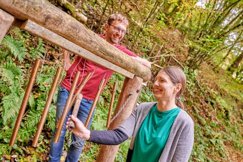 Zwei Personen an einem hölzernen Klangspiel im Wald.