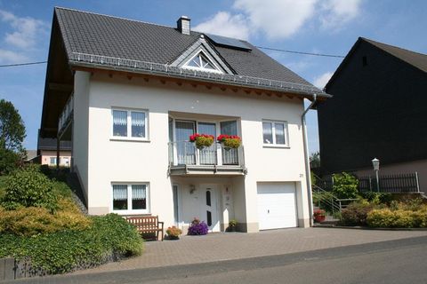 Ein helles Mehrfamilienhaus mit einem Balkon und Blumenkästen. Die Fassade ist freundlich gestaltet und von einem gepflegten Garten umgeben.