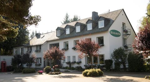 Ein gemütliches Gebäude mit einem einladenden Eingangsbereich. Umgeben von Bäumen und Blumensträuchern, strahlt es eine freundliche Atmosphäre aus.
