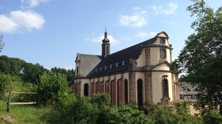 An old church surrounded by trees and green spaces. The sky is blue with some clouds.