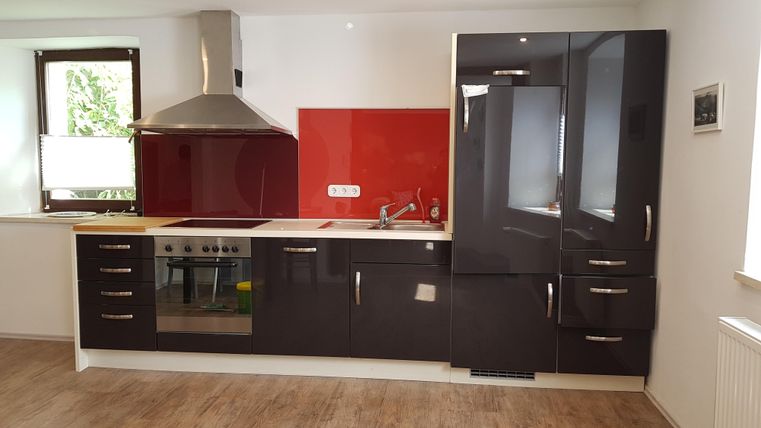 Moderne Küche mit schwarzen Möbeln und roter Rückwand. Gut beleuchtet und funktional gestaltet.