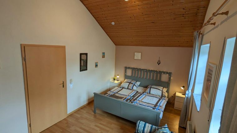 Ein gemütliches Schlafzimmer mit einem Holzofen und einem Doppelbett. Das Zimmer ist hell mit Holzdecke und modernen Möbeln eingerichtet.