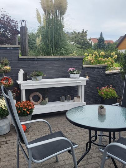 Ein gemütlicher Außenbereich mit einem Tisch und Stühlen. Viele Pflanzen und Blumen dekorieren die Umgebung.