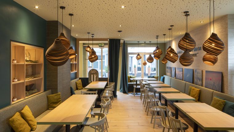 Ein modernes Café mit Holzdekor und gemütlichen Tischen. Sanftes Licht von hängenden Lampen schafft eine einladende Atmosphäre.