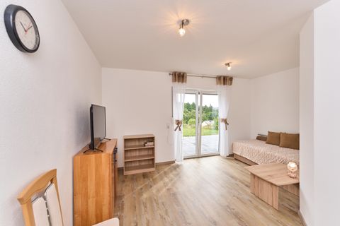 A cozy living room with a television, a table, and a sofa. Large windows offer a view of the nature-rich exterior.