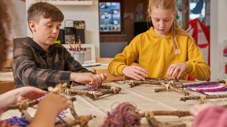 Kinder basteln an einem Tisch mit Naturmaterialien. Sie gestalten kreative Rahmen mit bunten Fäden.