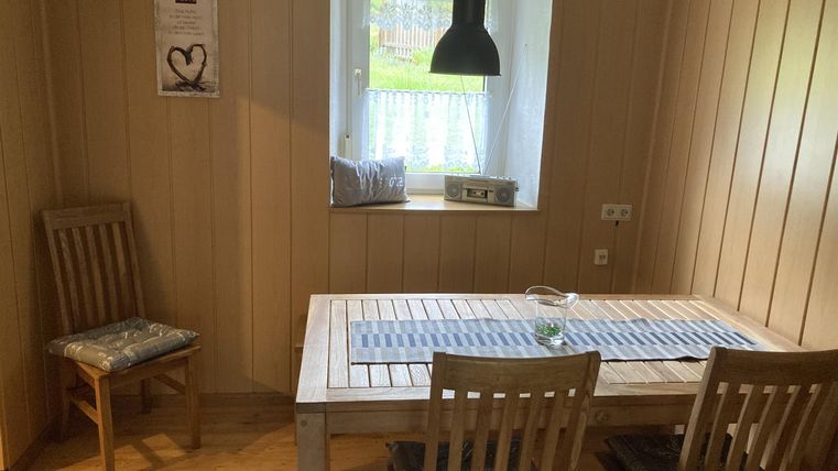 Ein heller Essbereich mit einem Holztisch und vier Stühlen. Die Wände sind aus Holz und ein Fenster mit Blick ins Freie sorgt für natürliches Licht.