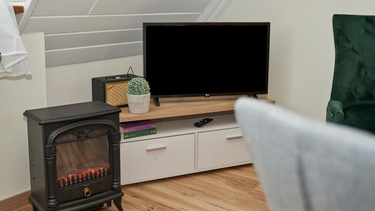 Ein gemütliches Wohnzimmer mit einem Fernseher und einem eleganten Kamin. Der Raum hat einen modernen Stil und einen warmen Holzboden.