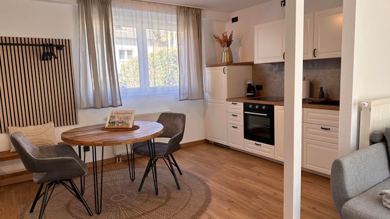 Ein gemütlicher Wohnraum mit einem runden Tisch und vier Stühlen. Die helle, moderne Küche ist gut ausgestattet und bietet viel Tageslicht.