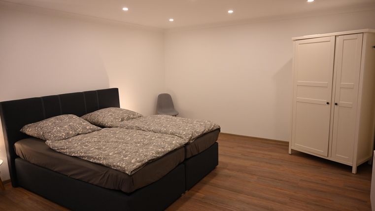 Ein modernes Schlafzimmer mit einem Doppelbett und einer bequemen Sitzgelegenheit. Der Raum hat helle Wände und einen schönen Holzboden.