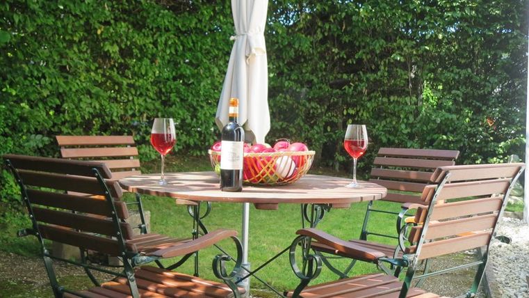 Ein einladender Tisch im Freien mit vier Stühlen. Auf dem Tisch stehen zwei Gläser Wein, eine Flasche Wein und eine Schale mit Äpfeln.