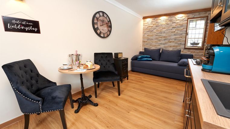 Ein gemütliches Wohnzimmer mit modernen Möbeln und Holzfußboden. Auf einem kleinen Tisch stehen Teegeschirr und zwei Stühle.