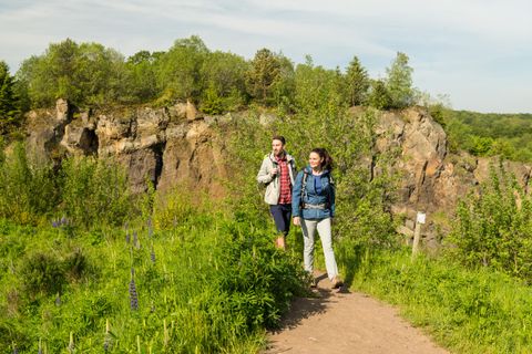 Two hikers on a path in the volcanic garden Steffeln, surrounded by green vegetation and rocks.