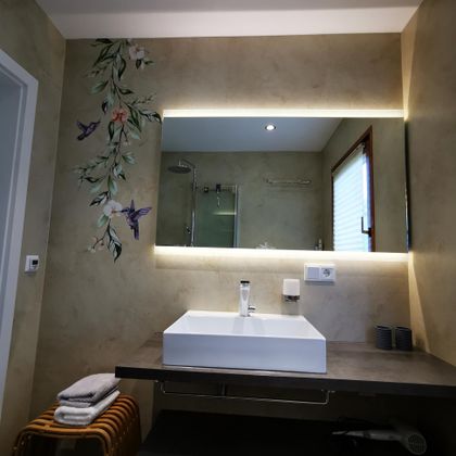 Ein modernes Badezimmer mit einem eleganten Waschtisch und einem großen Spiegel. Die Wände sind mit einer sanften Dekoration von floralen Motiven verziert.