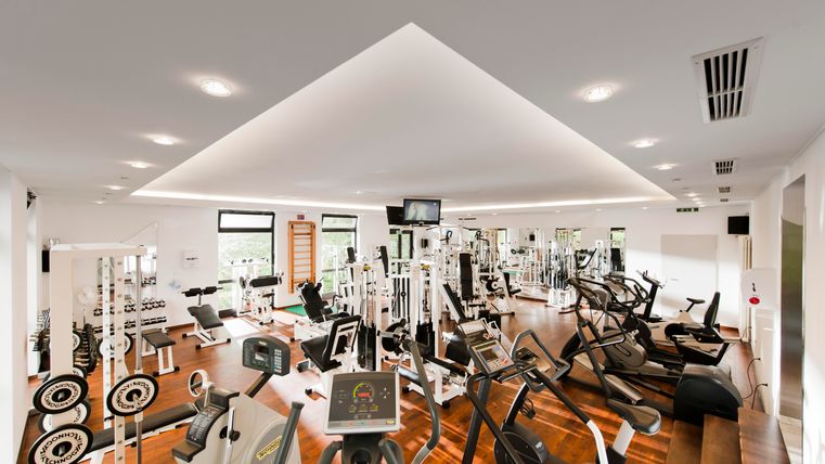 Ein modernes Fitnessstudio mit verschiedenen Trainingsgeräten und hellem Holzfußboden. Die Wände sind mit Fenstern für ausreichend Tageslicht ausgestattet.