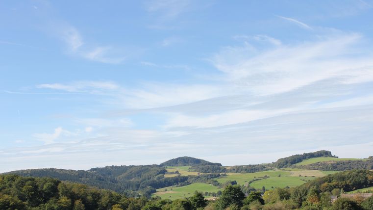 Eine malerische Landschaft mit sanften Hügeln und Wäldern. Der Himmel ist klar und blau, ideal für einen entspannten Tag in der Natur.