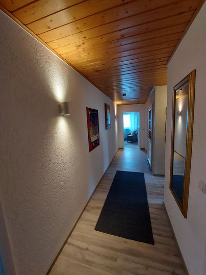 Ein schöner Flur mit Holzdecke und hellen Wänden. Am Ende des Flurs gibt es eine Tür, die zu einem hellen Raum führt.