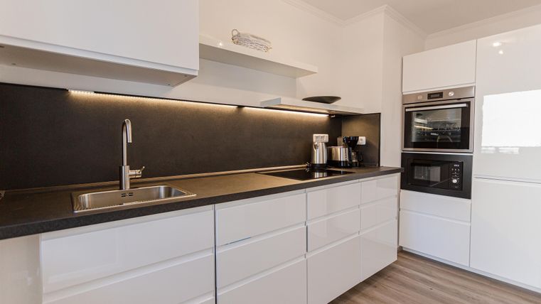 Moderne Küche mit weißen Möbeln und einer dunklen Arbeitsplatte. Sie ist mit hochwertigen Geräten und einem eleganten Design ausgestattet.