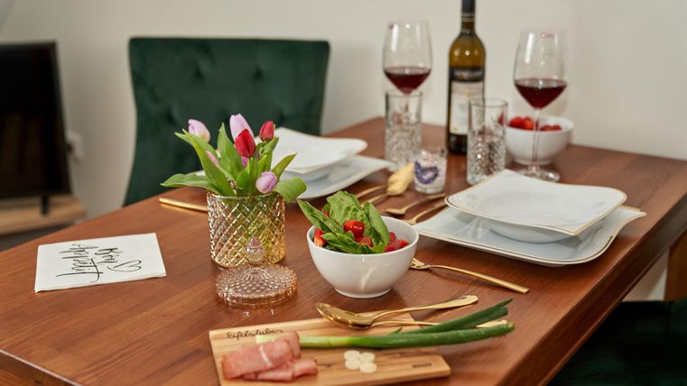 Ein schön gedeckter Tisch mit rotem Wein und frischen Blumen. Auf dem Tisch liegen Salat und appetitliche Zutaten bereit.